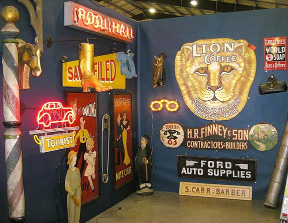 Bill Powell of Franklin, Tennessee, with his display of vintage signs is a show star sought out by regulars. Already sold were the large “Lion Coffee” face and the $2400 barber pole at extreme left. The glowing spectacles were $3800.