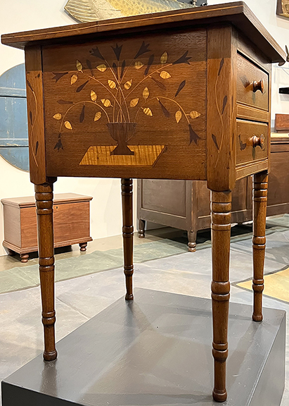 Newsom & Berdan Antiques & Folk Art, Thomasville, Pennsylvania, featured an 1810-30 two-drawer Pennsylvania stand with inlaid urns and foliage on both sides, vine inlay on the legs, and an anchor, fish, and diamond motifs for $12,500. String inlay was used along the edges of the top and drawers.