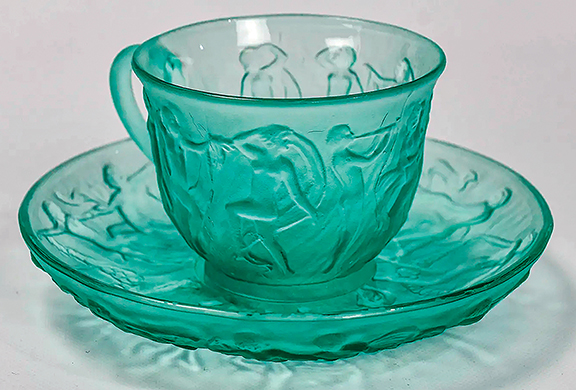 Here is a cup and saucer from a group that included two cups with saucers and two bread plates. The undamaged pieces in green are from the Consolidated Glass Company, and the Art Deco pattern is Dance of the Nudes or Dancing Nymph. The lot sold for $64 (est. $100/200).