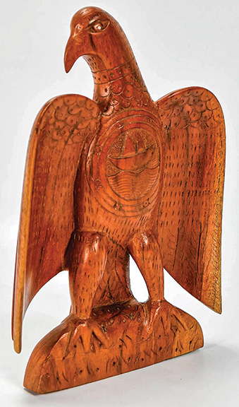 This spread-wing folk-art eagle is carved from a single plank of what appears to be mahogany. Dating from the early 20th century, it displays allover design enhancements and has a sailing ship within three concentric rings on the breast. The 12
