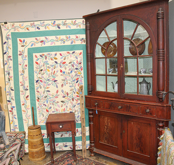 Quilt with a foliage design and double borders, 1930s or 1940s, $1925; wooden churn, $225; one-drawer drop-leaf stand in red paint, $275; peg rack, $215; two-piece architectural corner cupboard in grain paint, with bun feet, 50