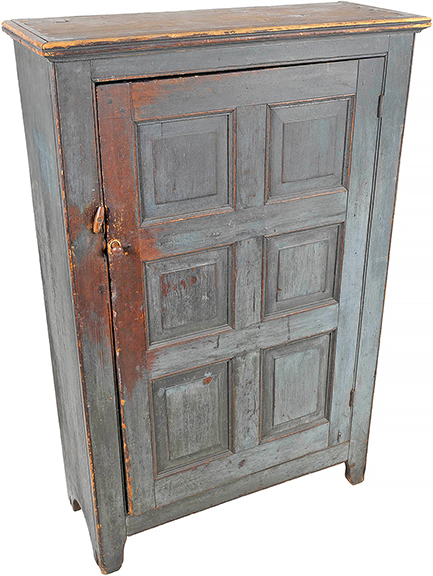 A Pennsylvania painted pine cupboard, possibly from Bucks County, circa 1820, retains much of its blue paint, revealing traces of a deep red-brown stain beneath. Below a molded cornice, the paneled door opens to three shelves. Measuring 54&frac12;