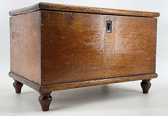 This miniature walnut blanket chest displays box-nailed construction, with the edges of the lid and bottom board rounded and slightly overhanging. The case is raised on turned peg feet. Its internal till appears to have never been fitted with a lid. The original lock and escutcheon are present, but the lid catch is missing. The little chest, 9