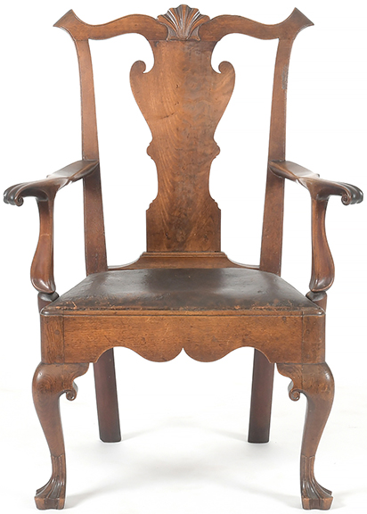 Delaware Valley carved walnut armchair, mid-18th century, formerly fitted with a chamber pot, with a Cupid’s-bow crest rail centered by a scallop shell above a figured solid splat, the outspread arms with knuckles and scrolled terminals, a trapezoidal leather-covered slip seat, a shaped front rail, volutes to the knee returns, raised on cabriole front legs terminating in trifid feet, the side rails having through tenons pinned into the raked back legs with stump feet, 41