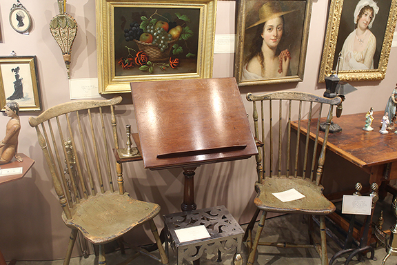 This grouping was found in the booth of Hanes & Ruskin Antiques, Niantic, Connecticut. The two Windsor chairs, circa 1800, retain much of their original apple-green paint. They were priced at $1450 the pair. The late 18th-century mahogany music or library stand features an adjustable top and two candle slides. It was also tagged $1450. The brass and iron footman is British and was marked $950. The still life of a fruit basket with roses is signed “E. Steele,” likely Edwin Steele (British, 1803-1871). It was priced at $2600.