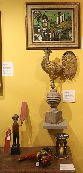 This array of Americana was found in the booth of Blandon M. Cherry Antiques and Art, Paris, Kentucky. The gold-leaf rainbow-tail rooster, mounted on a turned and painted wooden post finial, dates from the late 19th century. It was priced at $12,500. The oil on board by artist/poet Henry L. Faulkner (1924-1981), Taormina [Sicily] Cityscape, was priced at $35,000. The painted wooden hourglass was $1900; the carved and painted cornucopia, $3700; and the figural whirligig, $2500.