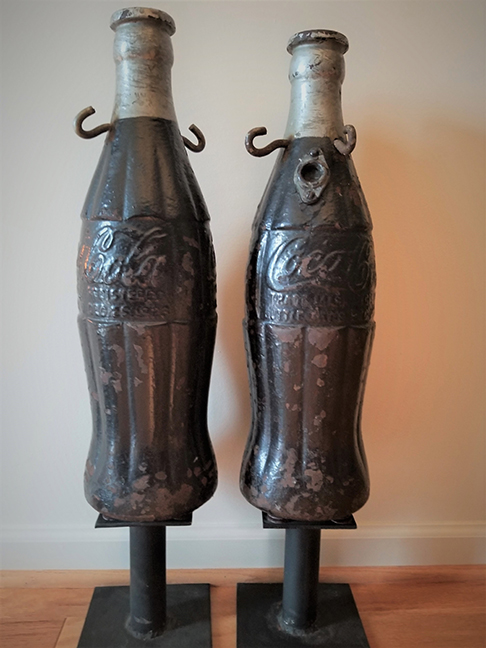 These cast-iron bottles were used at a Baltimore, MD, bottling plant as fence finials. In very good condition with no repairs. American, c.1920. Bottle resting on metal bases for display. The bottles have raised Coca-Cola lettering and Pat. Date Dec. 25, 1923. The bottles have hooks for fence chains to be attached. 20